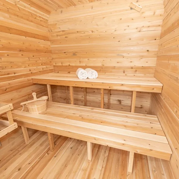 Cube sauna interior in knotty cedar with two-tier benches across the rear wall, rolled towels, wooden bucket and ladle.