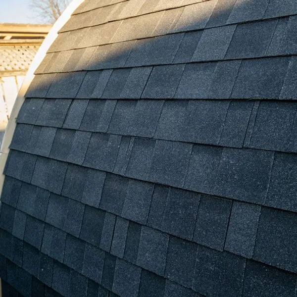 Close-up of dark grey asphalt shingles on the curved roof of a pod sauna.
