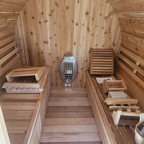 Barrel sauna interior in knotty cedar: benches both sides, backrests, headrests and electric heater with guard on the rear wall
