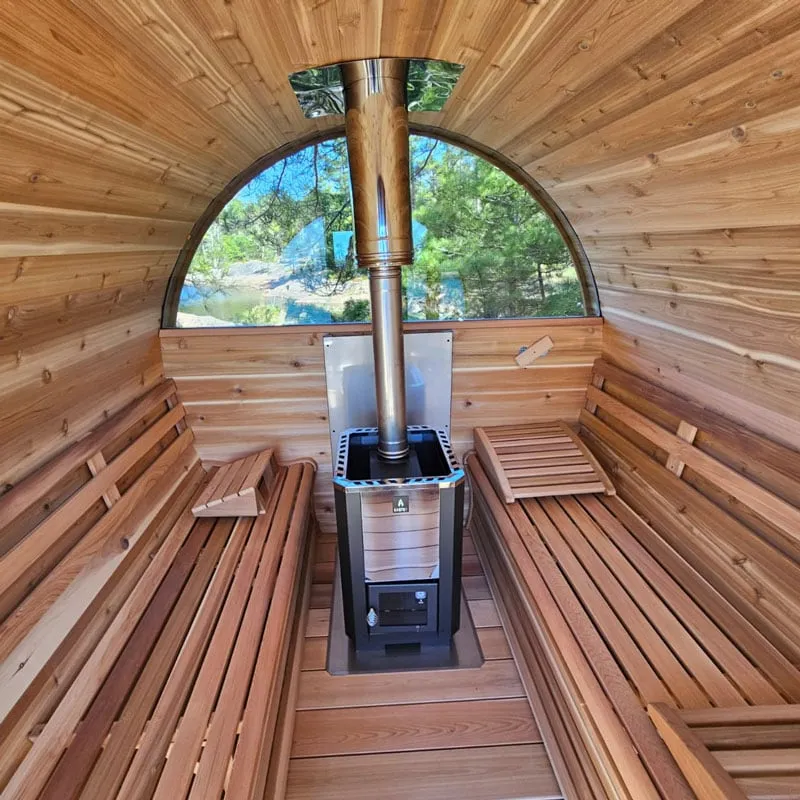 Barrel sauna interior with wood-burning stove and stainless flue, cedar benches both sides, half-moon rear window to forest and water