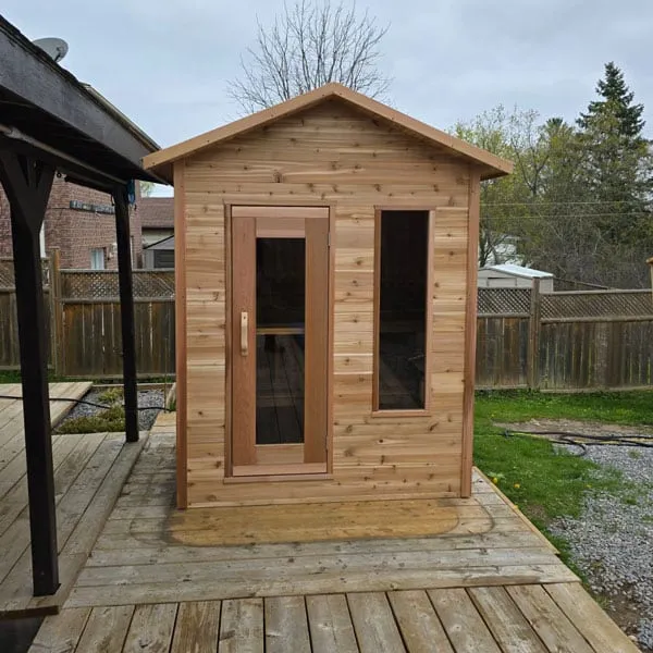 Cedar cabin sauna with gabled roof, glass-panel door and side window on a timber deck in a fenced backyard