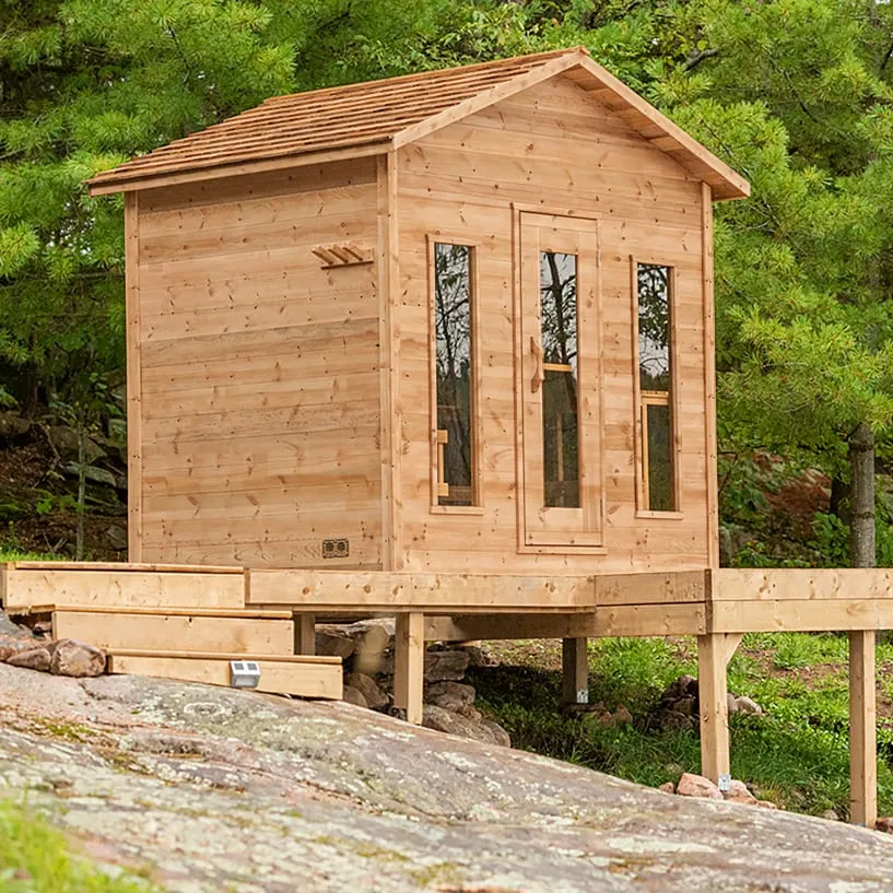 Cedar cabin sauna with shingle roof, glass door, two narrow windows and towel pegs on a raised deck above granite rock