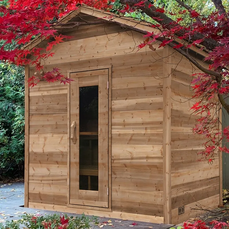 Gabled cedar cabin sauna with glass-panel door under red maple leaves, vent near the base