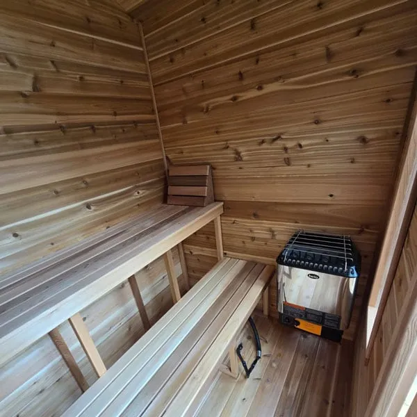 Cabin sauna interior: two-tier cedar benches, headrest and stainless electric heater with rock grille in the corner