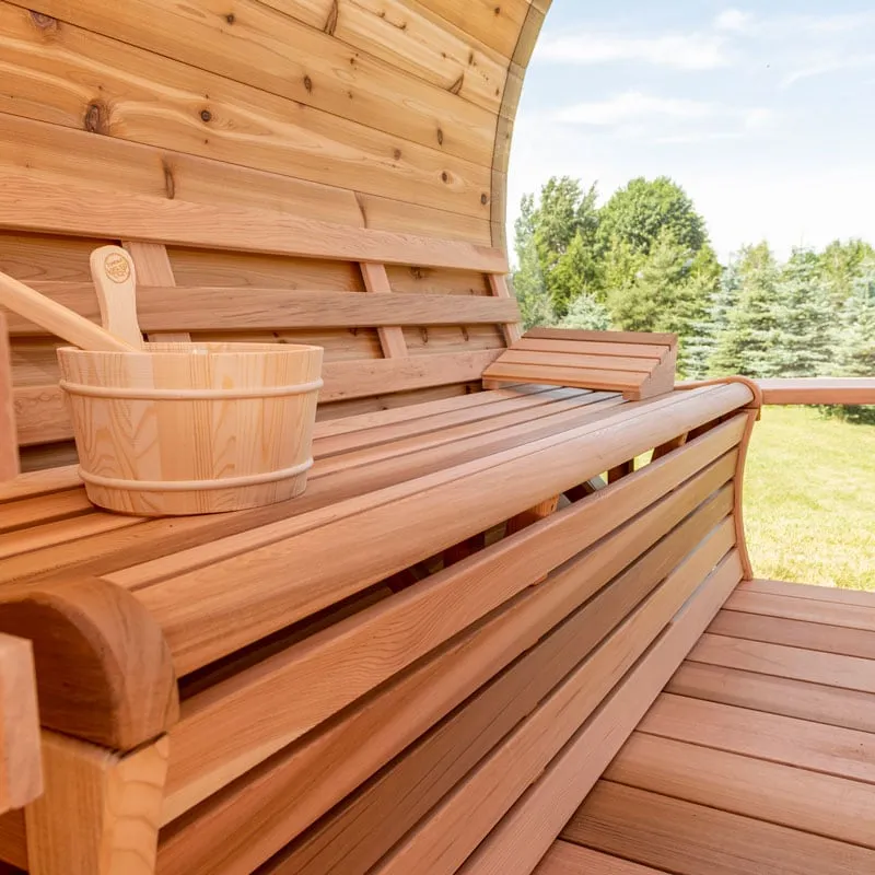 Close-up of cedar bench with backrest, wooden bucket, ladle and headrest inside a barrel sauna, glass end view to lawn