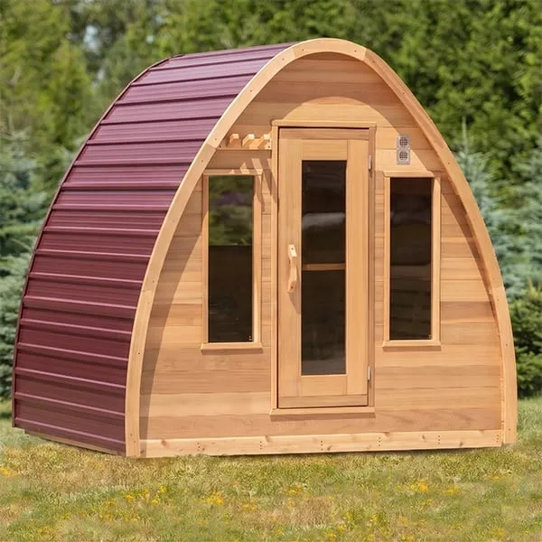Pod sauna with burgundy metal roof cladding, cedar front, glass door and two side windows, on a lawn with trees