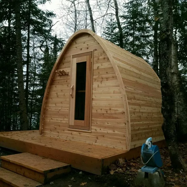 Knotty cedar pod sauna with glass door and towel pegs on a raised timber deck with steps in woods