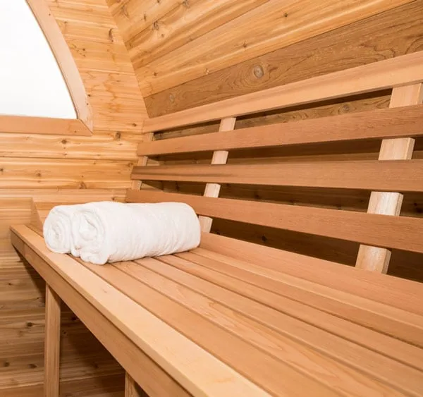 Pod sauna interior: cedar bench with slatted backrest and rolled towel beside an arched window