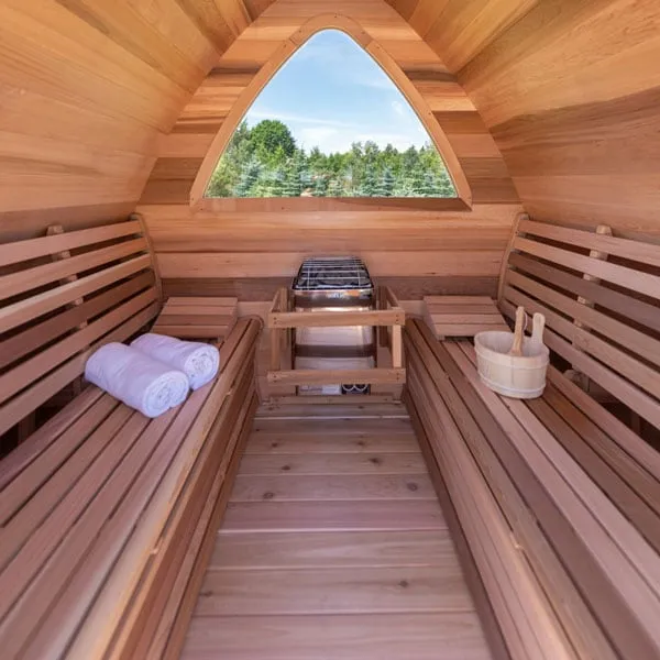 Pod sauna interior: cedar benches both sides, electric heater with timber guard below arched rear window, towels and bucket