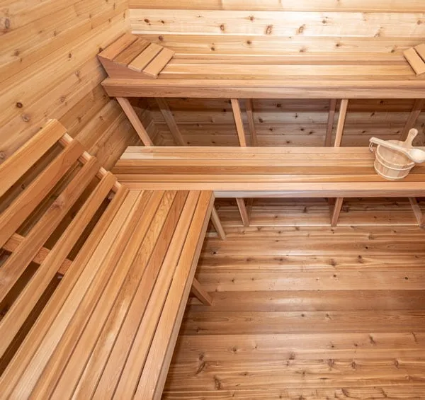 Overhead view of two-level L-shaped cedar benches inside a sauna, with bucket and ladle