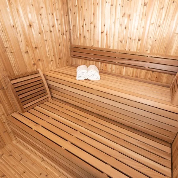 Knotty cedar sauna interior with two-tier L-shaped benches, backrest and rolled white towels