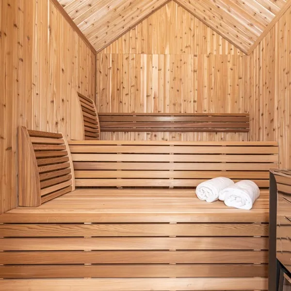 Knotty cedar sauna interior under a peaked gable ceiling, with two-tier benches, backrests and rolled towels