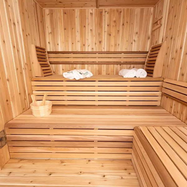 Sauna interior with knotty cedar walls, two-tier cedar benches with backrests, rolled towels and a wooden bucket