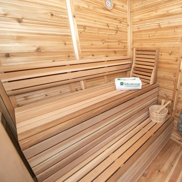 Sauna interior with horizontal knotty cedar walls, two-tier cedar benches, backrest, folded towel, wooden bucket and wall clock